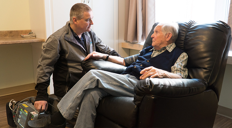 Caregiver checking senior's heart rate with portable ECG machine